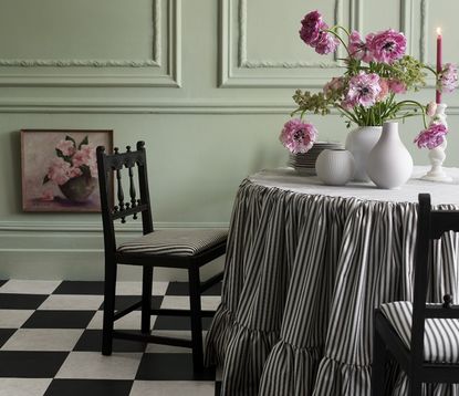 A dining room with a checkerboard flooring and ticking stripe upholstered chairs and tablecloth