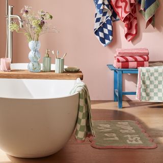Pink bathroom with a bathtub and colourful, patterned towels and bath mat