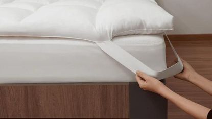 A hand pulling the corner strap of the Coop Retreat Mattress Topper over a mattress.