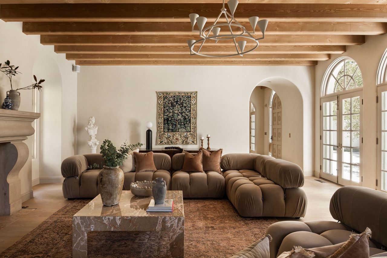 A living room with a large, L-shaped sofa and a plaster chandelier 