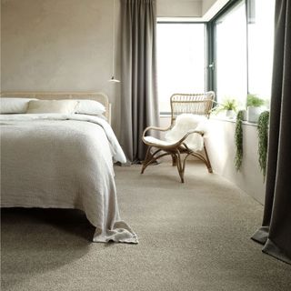 neutral bedroom with pale neutral carpet, beige walls and a wicker chair and headboard