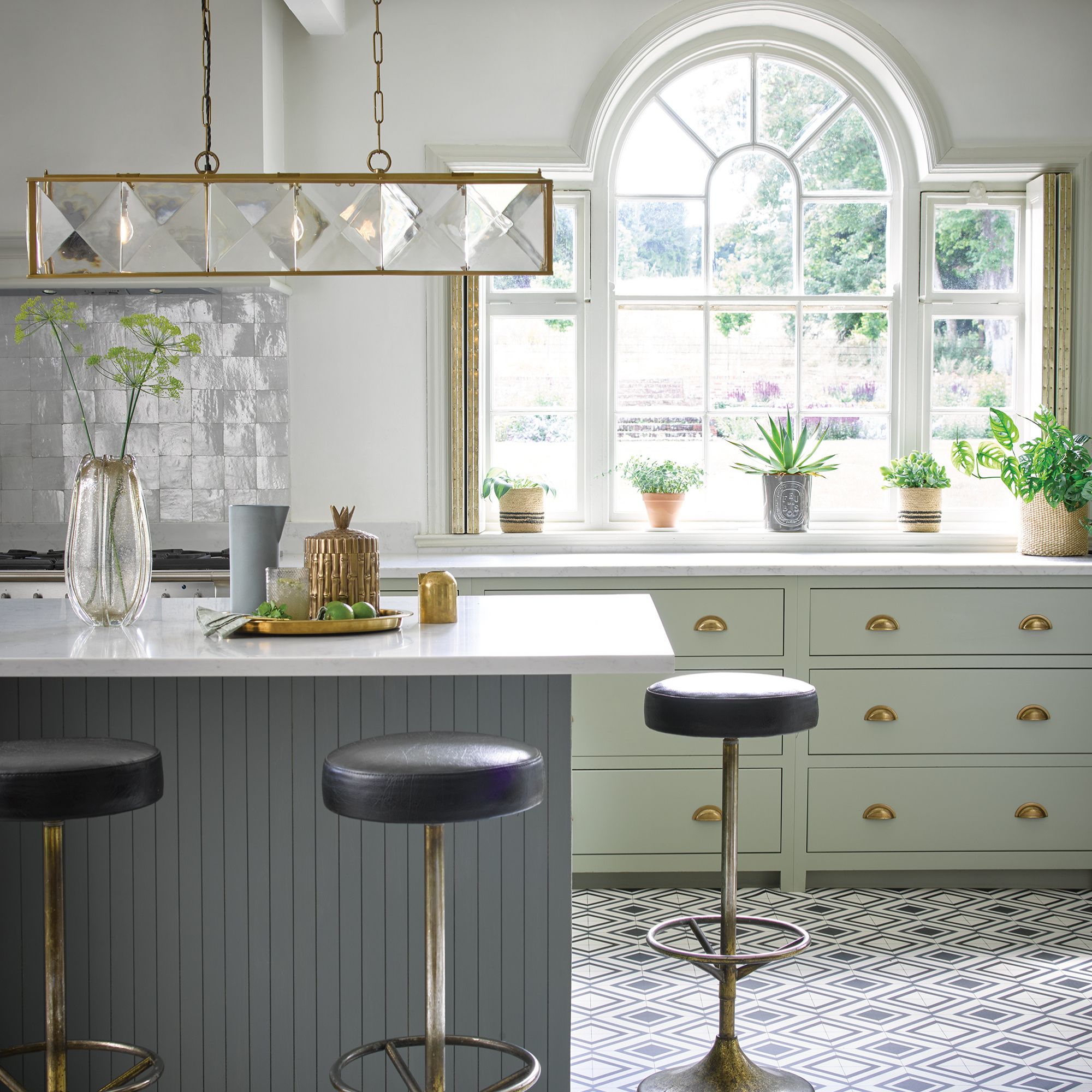 pendant light above isladn in grey and green kitchen with feature window and upholstered bar stools