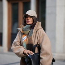 cold weather skincare F&uuml;sun Lindner is seen wearing a beige baseball cap with minimal branding from Canada Goose; an oversized checked scarf in muted earthy tones, with a soft and fluffy texture from Acne; 
