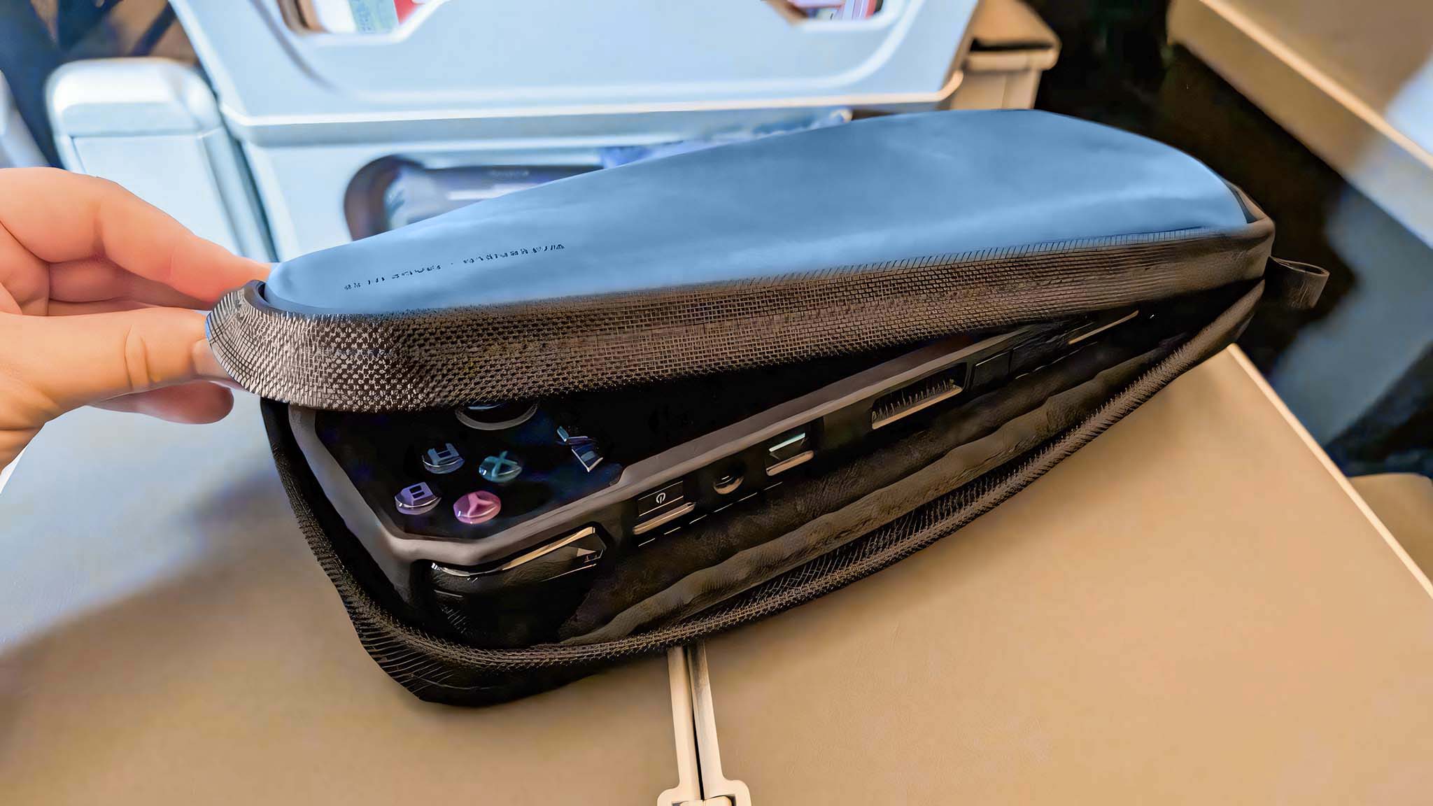 A hand holding the Waterfield ROG Ally X Magnetic Case open on an airplane tray to view the Ally X inside.