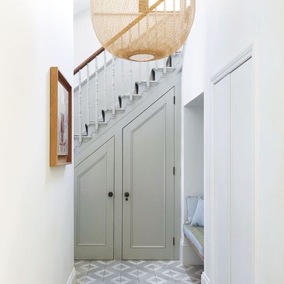 White painted hallway with a wooden staircase at the end, and an under-the-stairs cupboard underneath