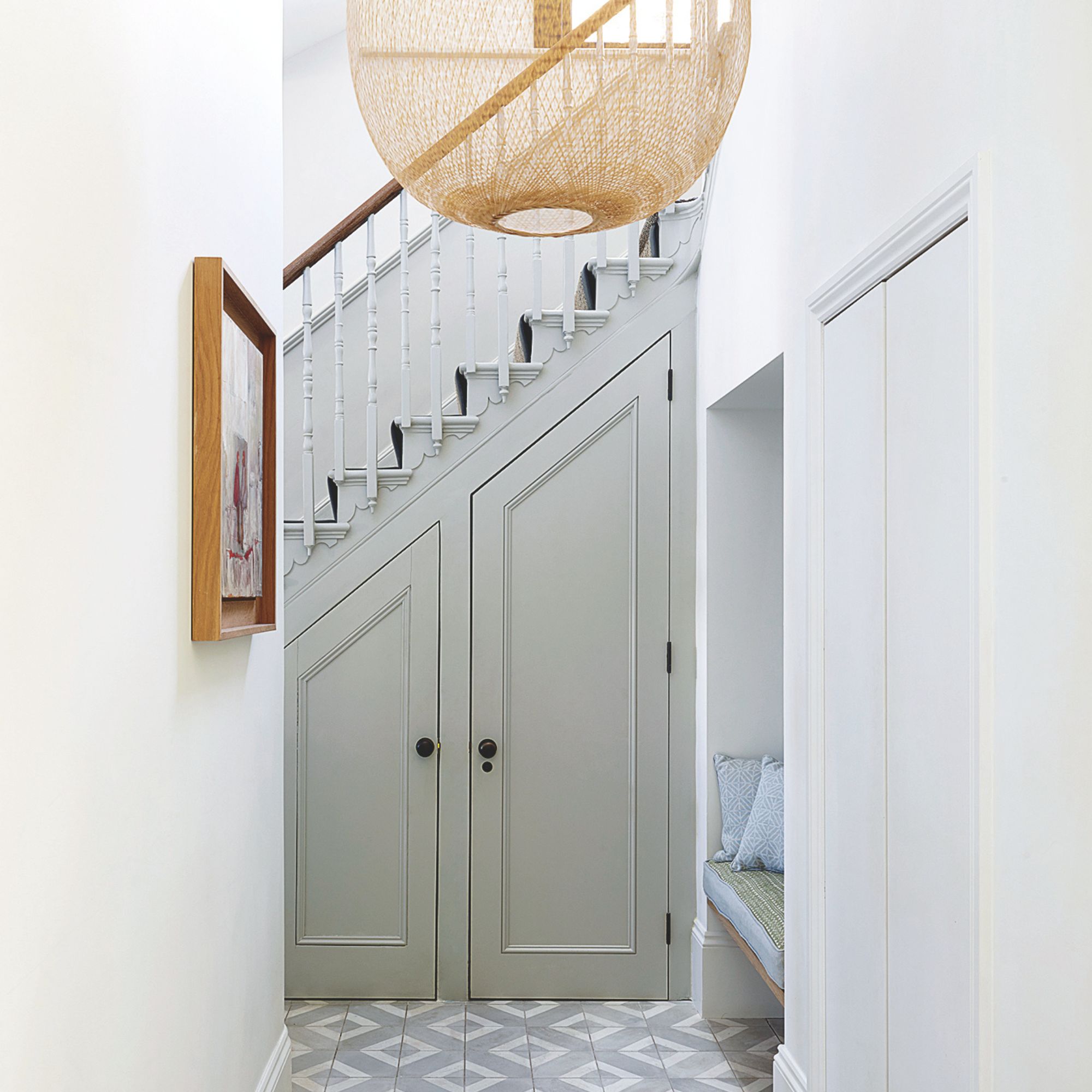 White painted hallway with a wooden staircase at the end, and an under-the-stairs cupboard underneath