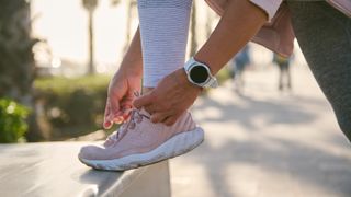 Woman fastening running shoes while wearing sports watch