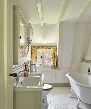 cottage bathroom with sloping ceiling, claw foot bath, floral curtain at window and hexagonal floor tiles