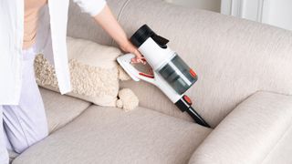 A cordless vacuum cleaner being used as a handheld to clean the couch