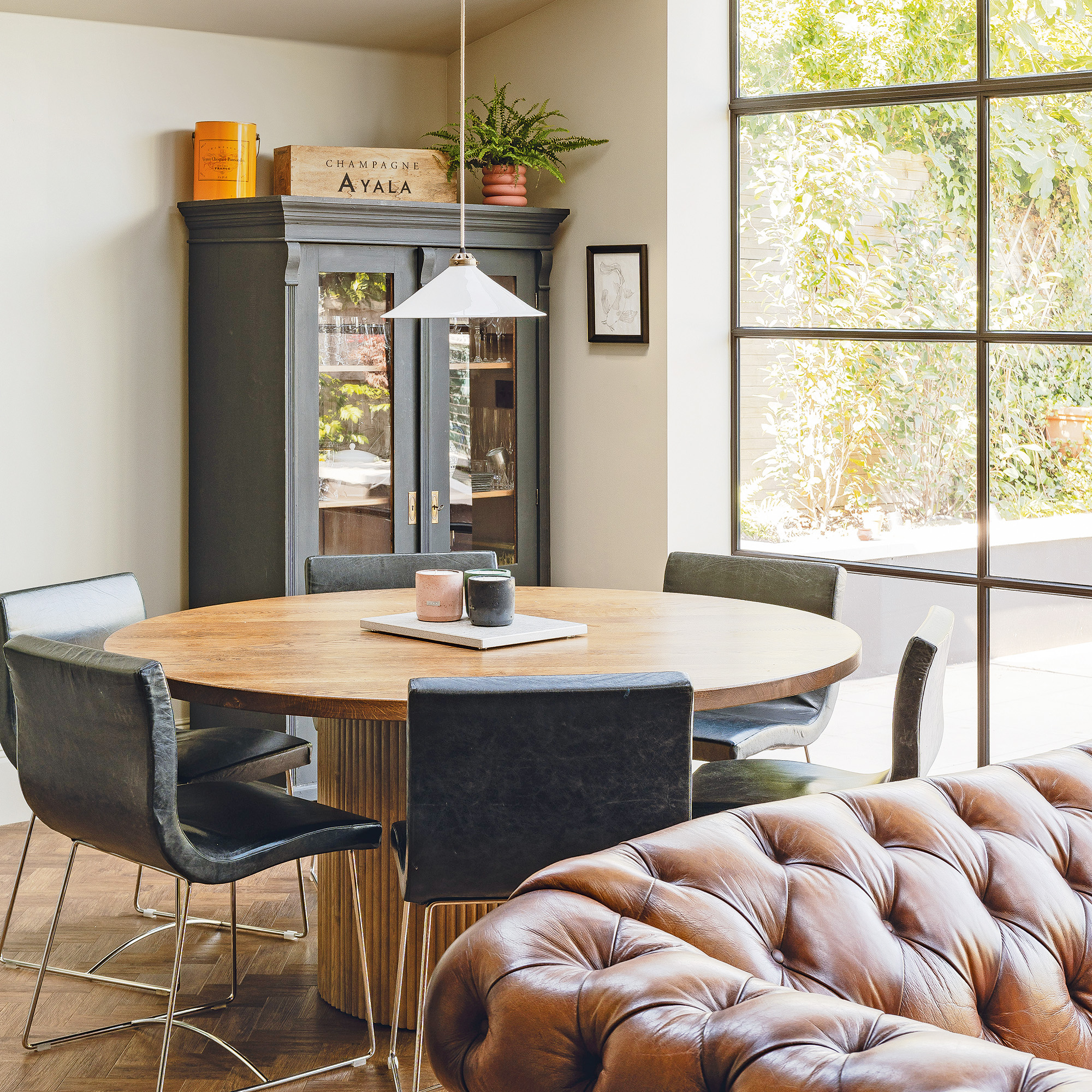 wooden circle table with five chairs and black glass cabinet in corner with glass crittall patio doors