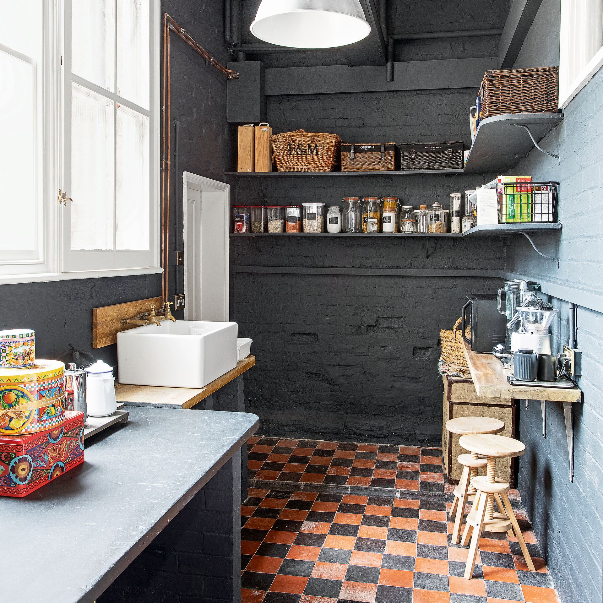 Laundry room with brick walls painted dark grey, terracotta and black tiled flooring and open storage