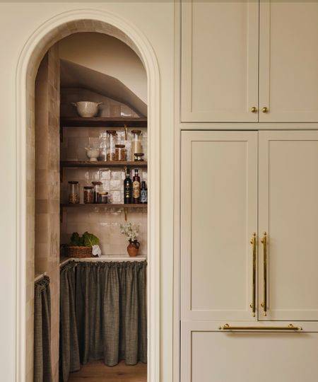 A neutral kitchen with an arched entry into a pink tiled kitchen larder