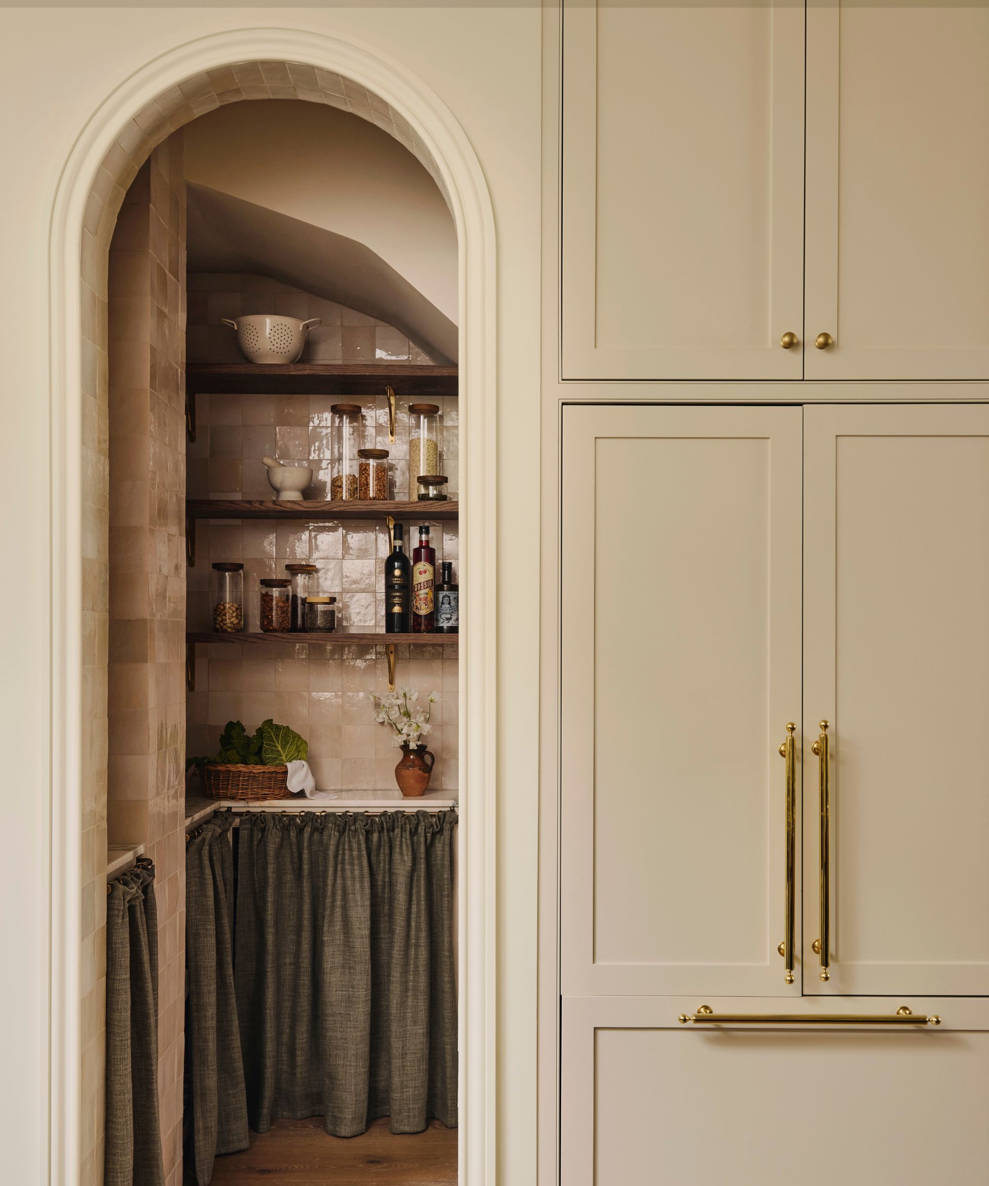 A neutral kitchen with an arched entry into a pink tiled kitchen larder