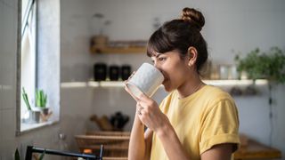 A woman wearing a yellow tshirt drinking a hot beverage