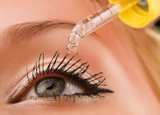 A woman holds an eye dropper full of liquid above her eye.