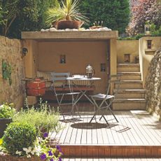 A garden with a grey bistro set and a built-in bench under a covered area