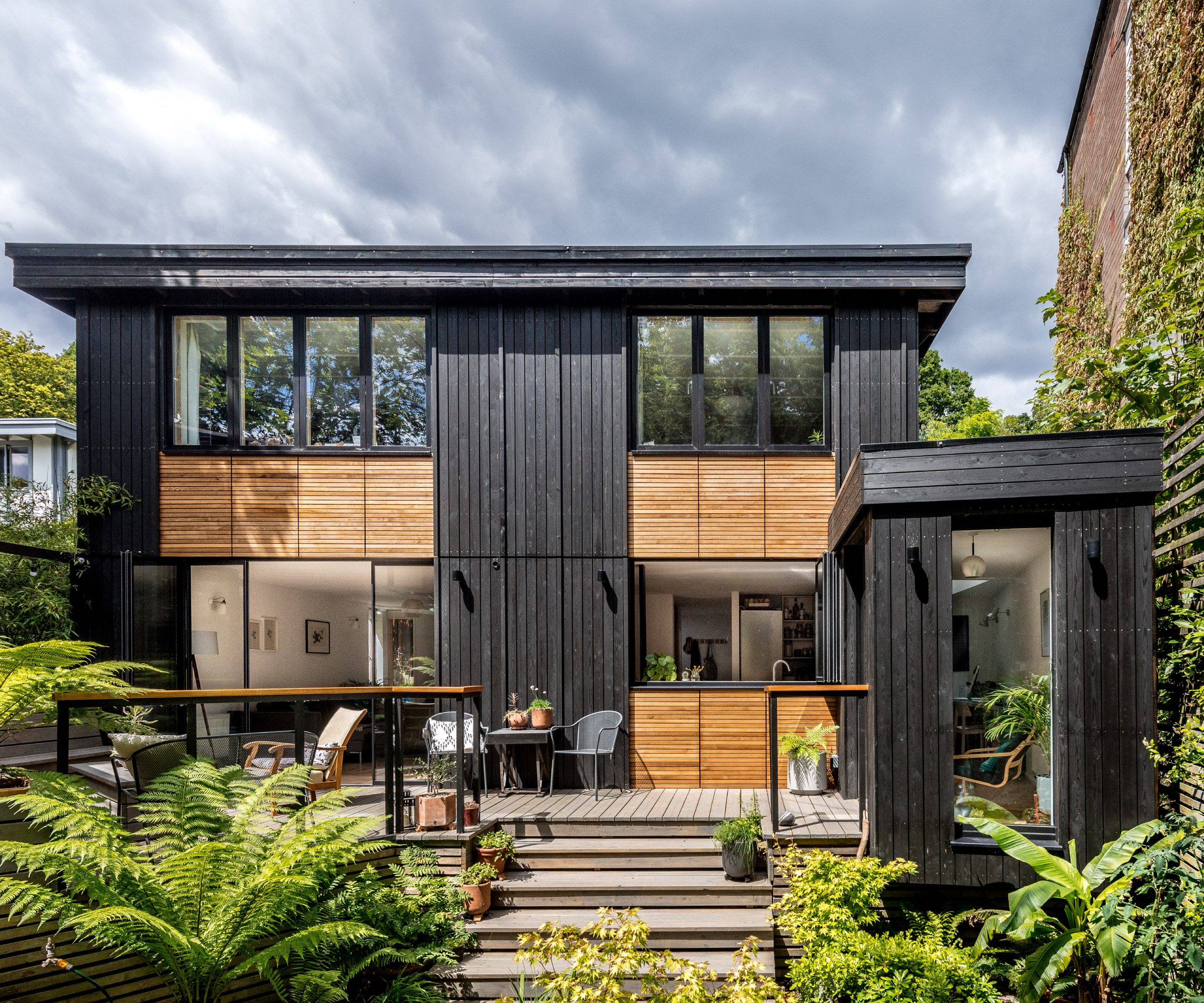 rear of house completely clad in black and oak wood strips leading to lush green garden and patio