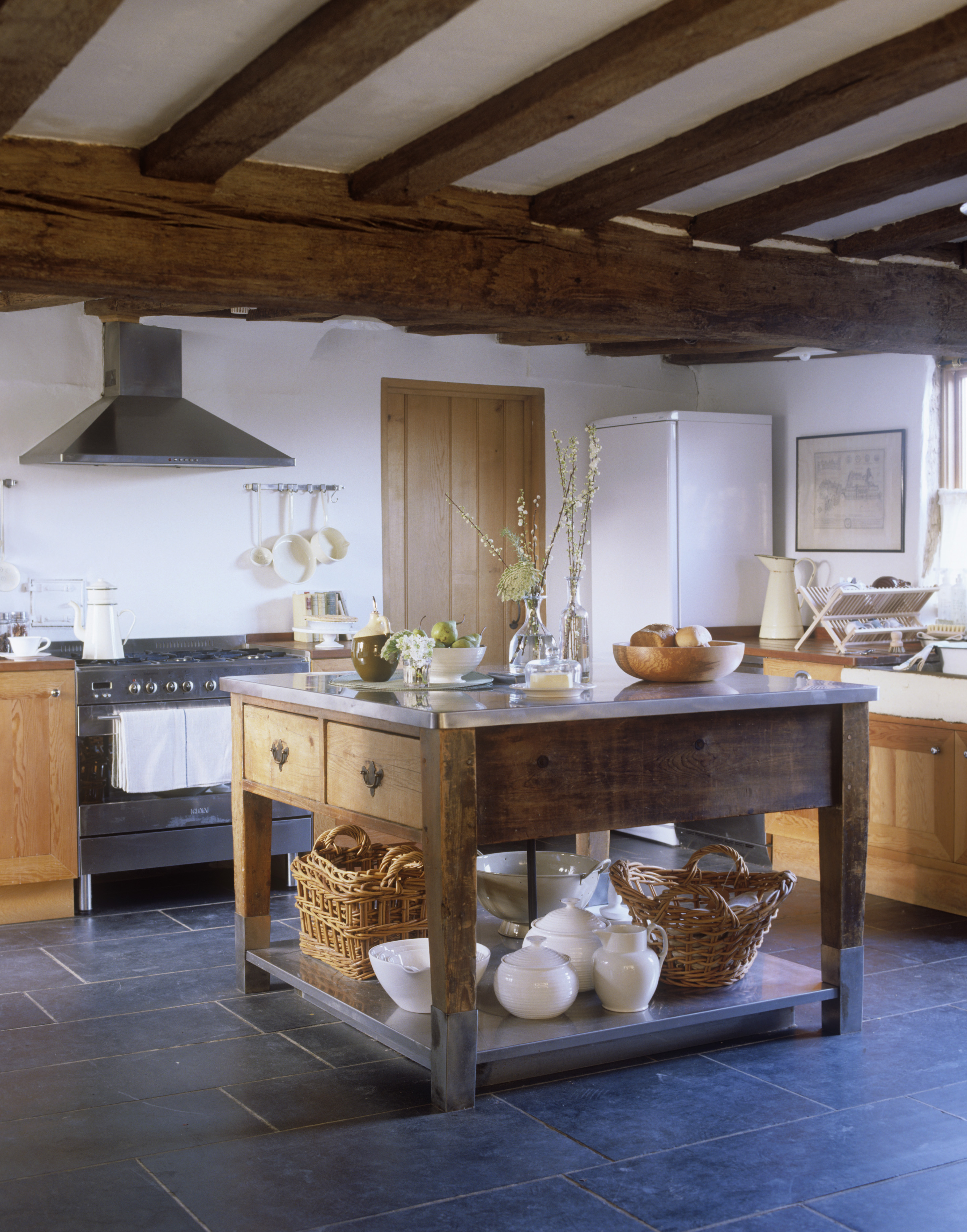 A rustic wooden portable kitchen island in a farmhouse kitchen with dark gray slate flooring.