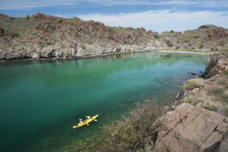 Kayakers paddling on turquoise waters surrounded by rugged cliffs in Loreto, Mexico, under a clear blue sky.