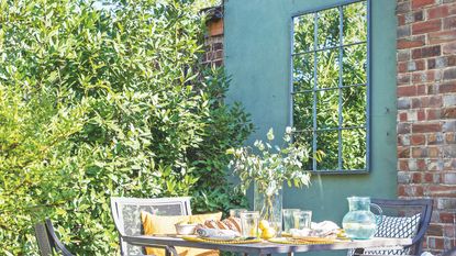 Garden mirror on painted blue outdoor wall behind garden seating area