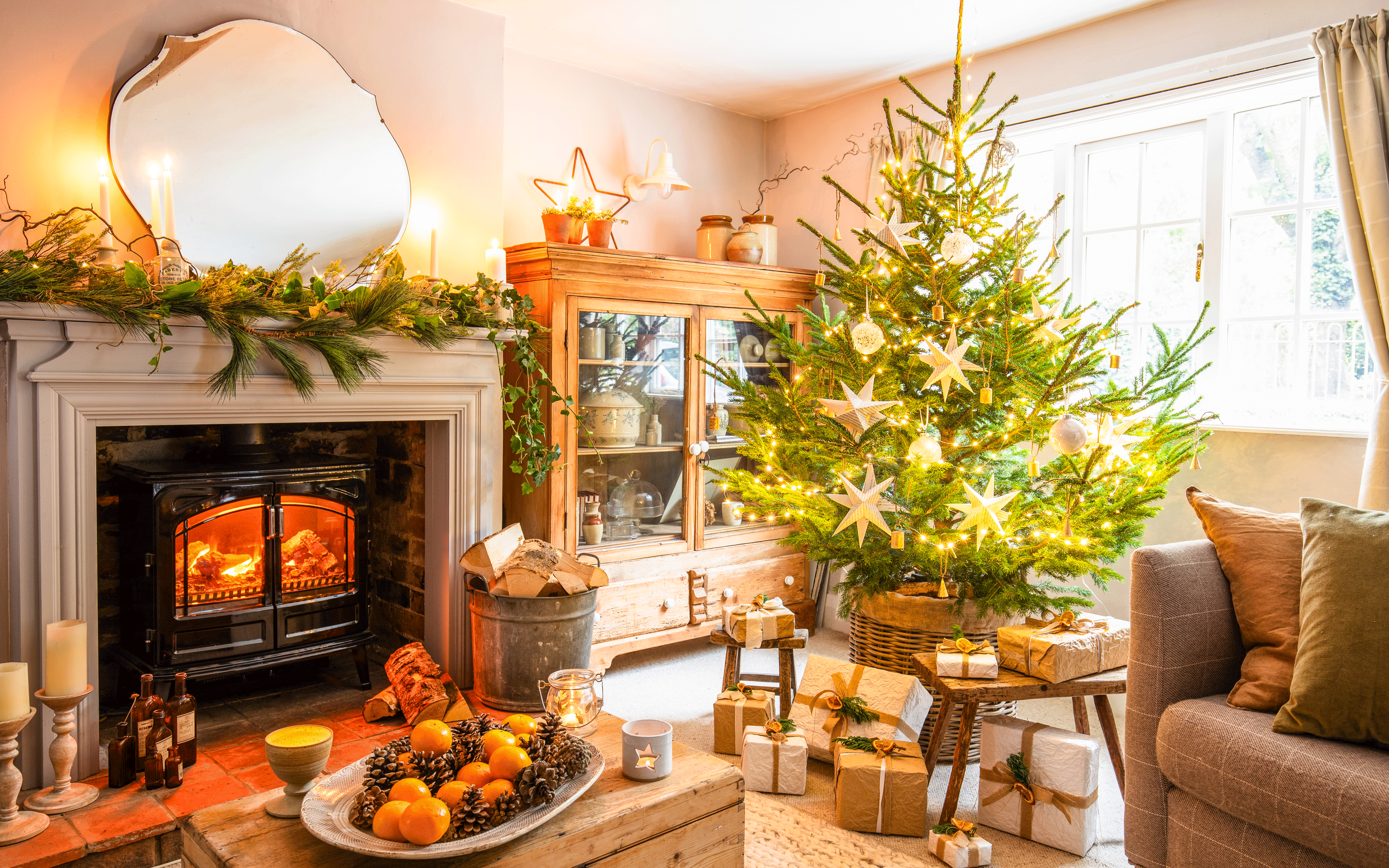 a living room with a fireplace surround with a faux woodburner decorated for Christmas and a Christmas tree