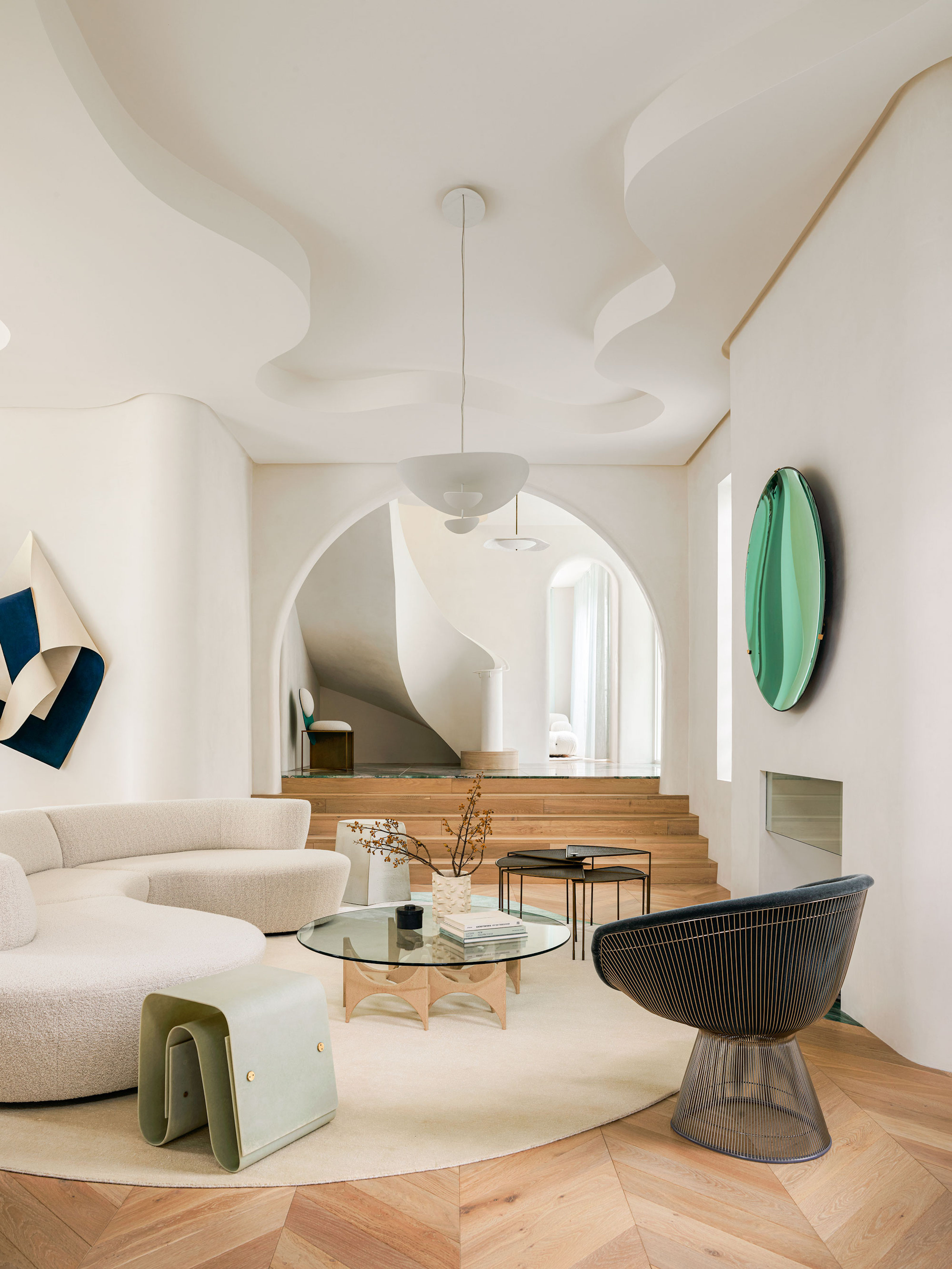 A white, spacious living area with a view through a arched stairway to the entryway, and all modern style furniture in the living space.