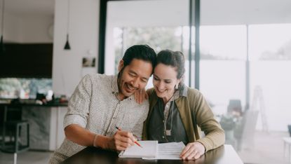 A couple go over a checklist and documents at their dining room table.