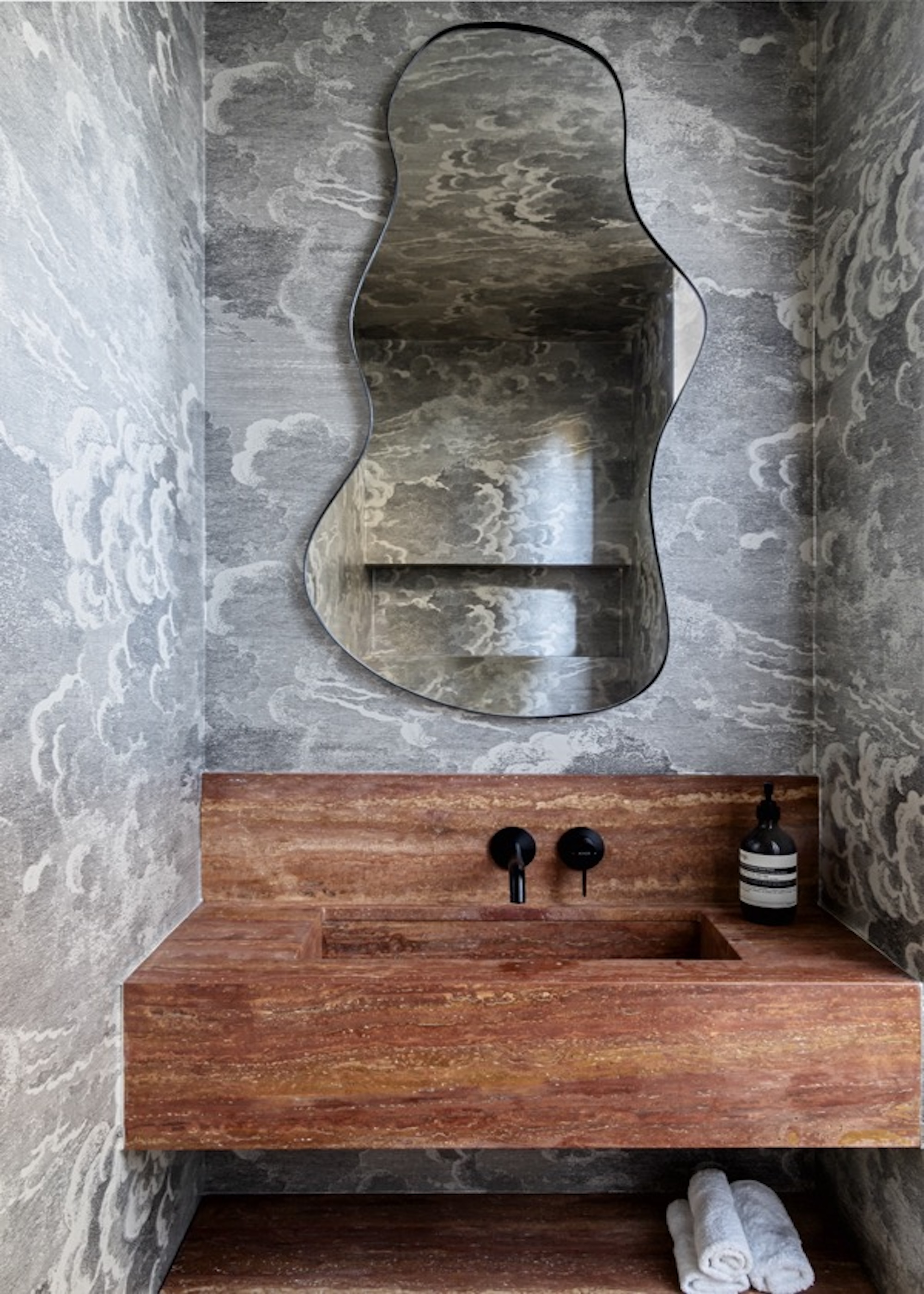 A bathroom with a curvy mirror as well as a red colored basin sink and grey wallpaper