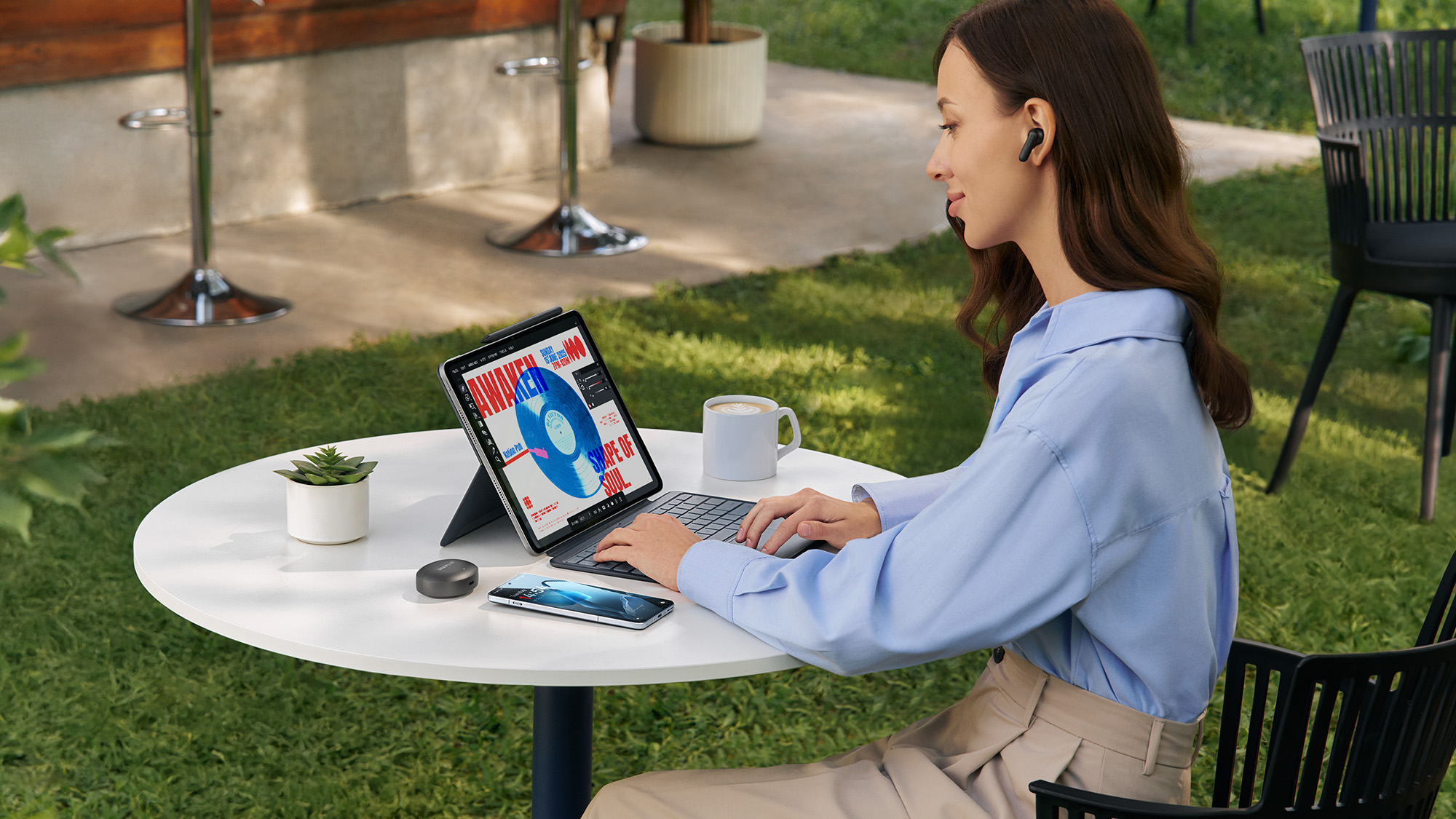 OnePlus Pad 3 lifestyle image being used by person in garden on a table next to phone, coffee cub and pot plant