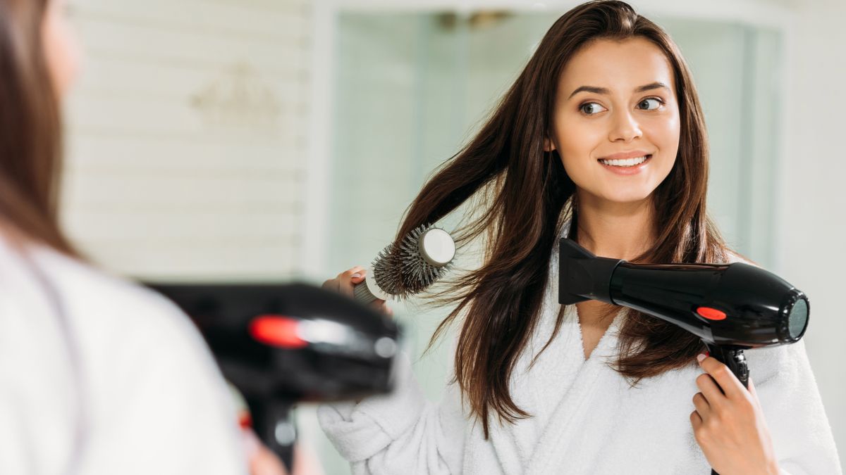 Woman blow drying her hair in front of a mirror