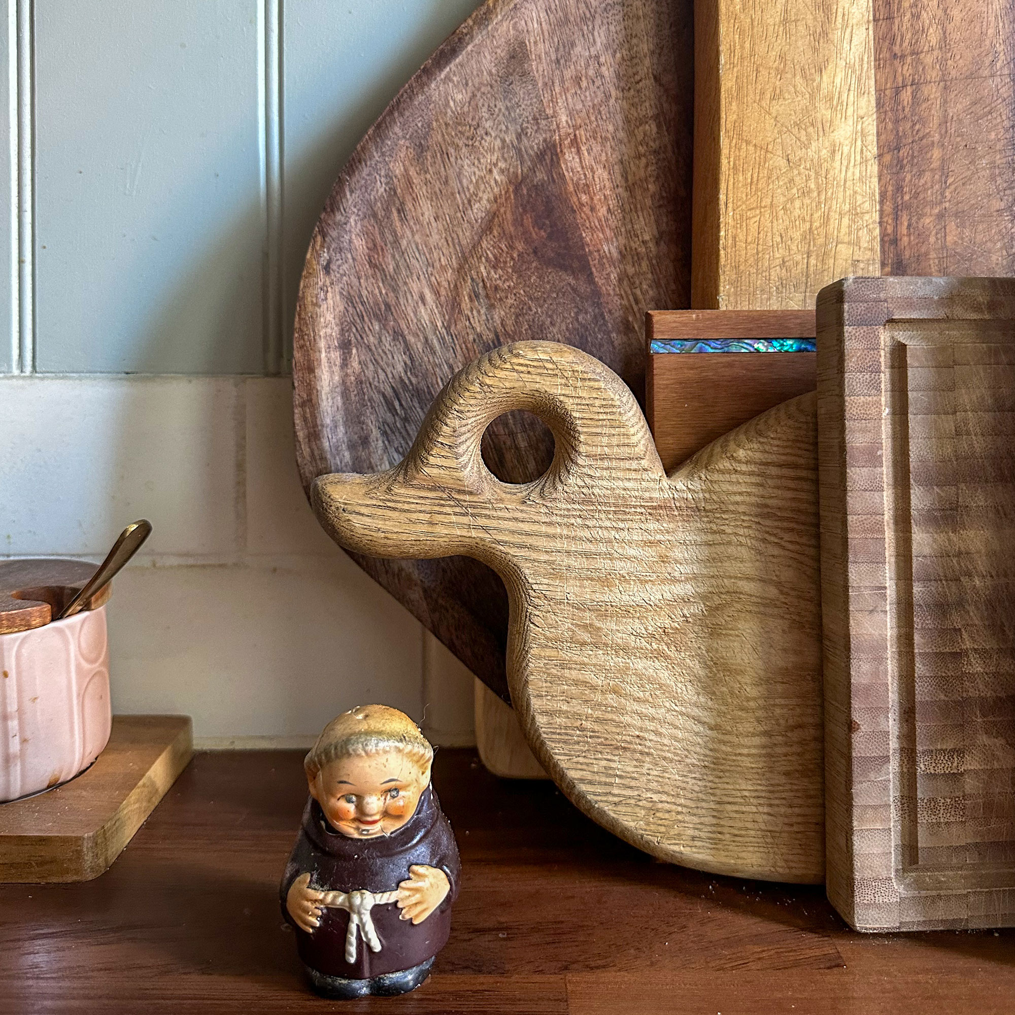 Small monk ornament on wooden countertop in front of stack of wooden chopping boards, including one shaped like a duck