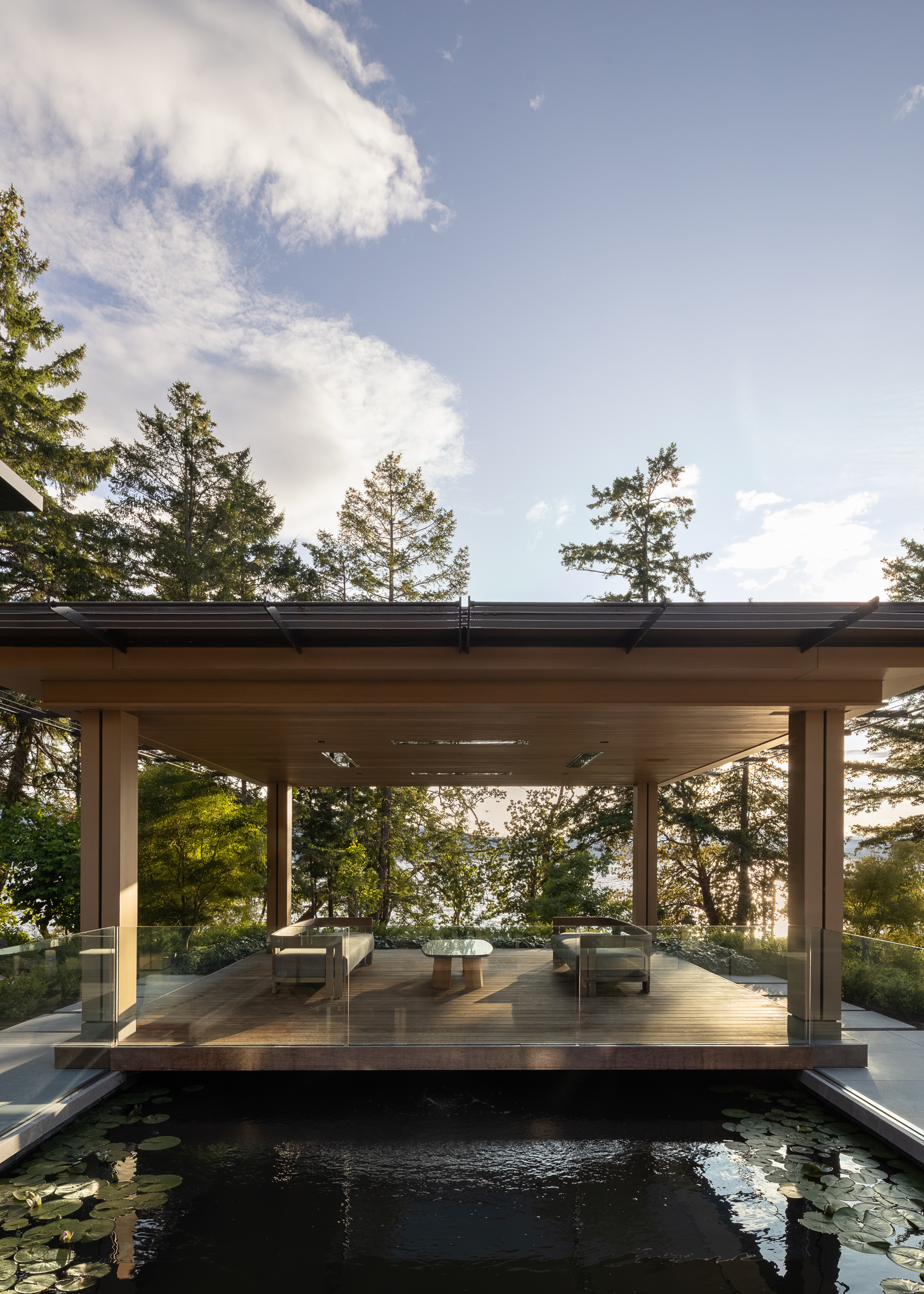 a covered pergola with a sofa and table sits over a pond