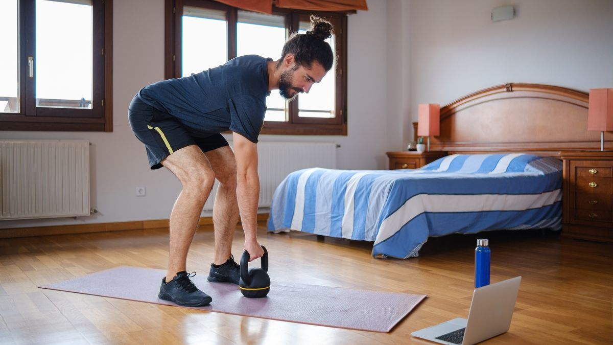 Man leaning over to hold kettlebell on the floor, the starting position for the kettlebell clean