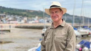 Michael Portillo stands in a harbour in Great Coastal Railway Journeys series 3