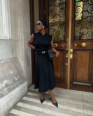 Woman wears black top, black skirt, black shoes