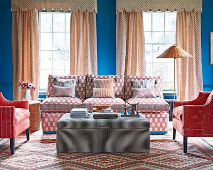 Valances vs pelmets vs swags vs cornices: A living room curtain idea with blue walls, red and white sofa, and cream curtains with pelmet