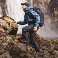 Hiker clicking up a boulder infront of a waterfall wearing Helly Hansen outdoor clothing and a rucksack