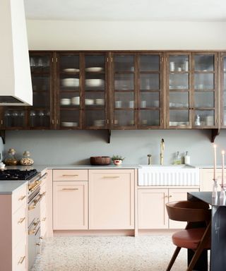 A kitchen with pink lower cabinets and wooden see through upper cabinets