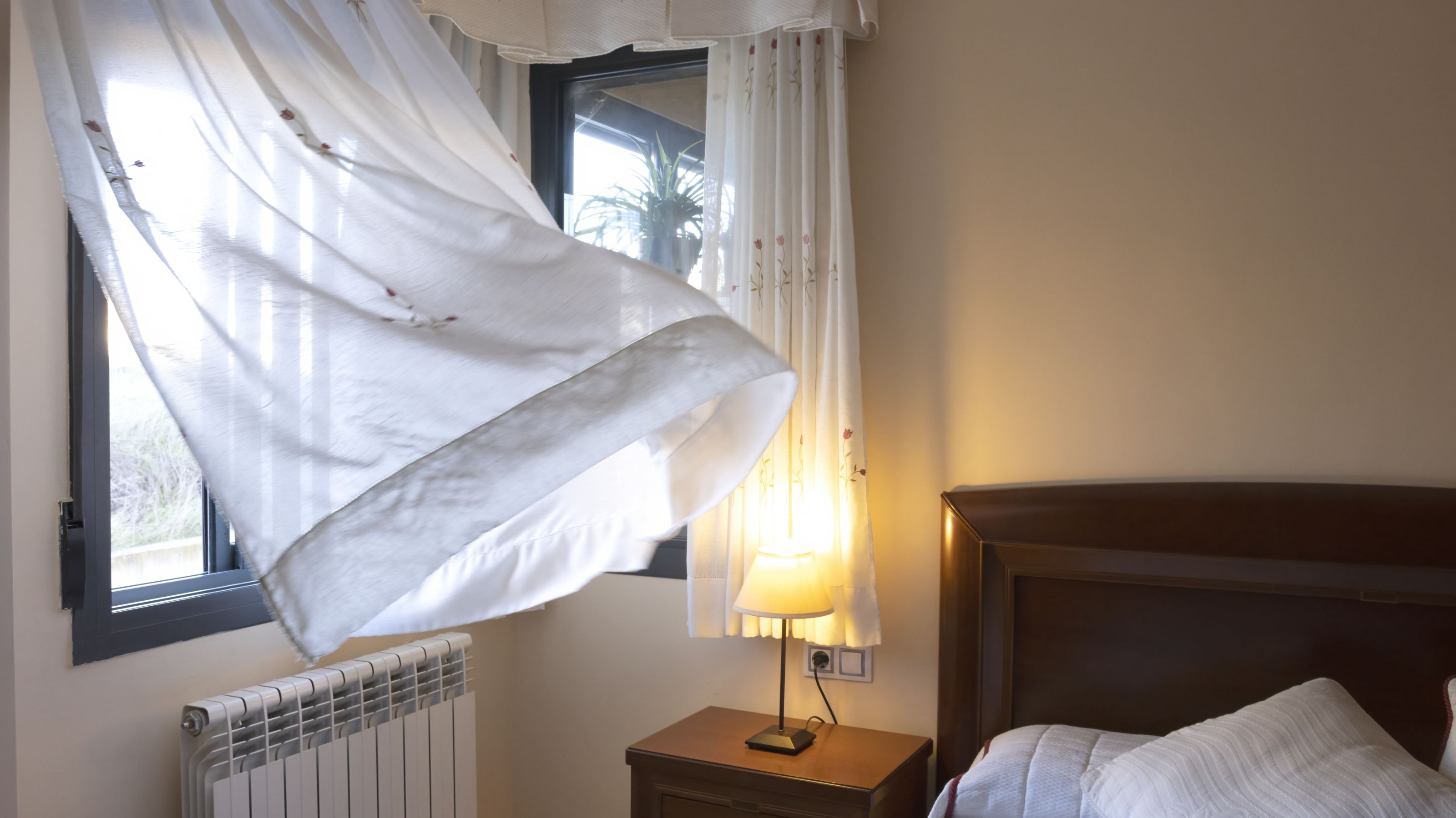 Open window in bedroom with sheet curtain billowing in the breeze
