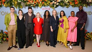 The cast of Bridgerton season 3 standing in a line for photographers in front of a branding board for Netflix