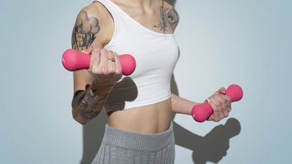 Mid section of Young Woman With tattoo practicing Fitness and Dumbbell Weights on white Background.Studio shot