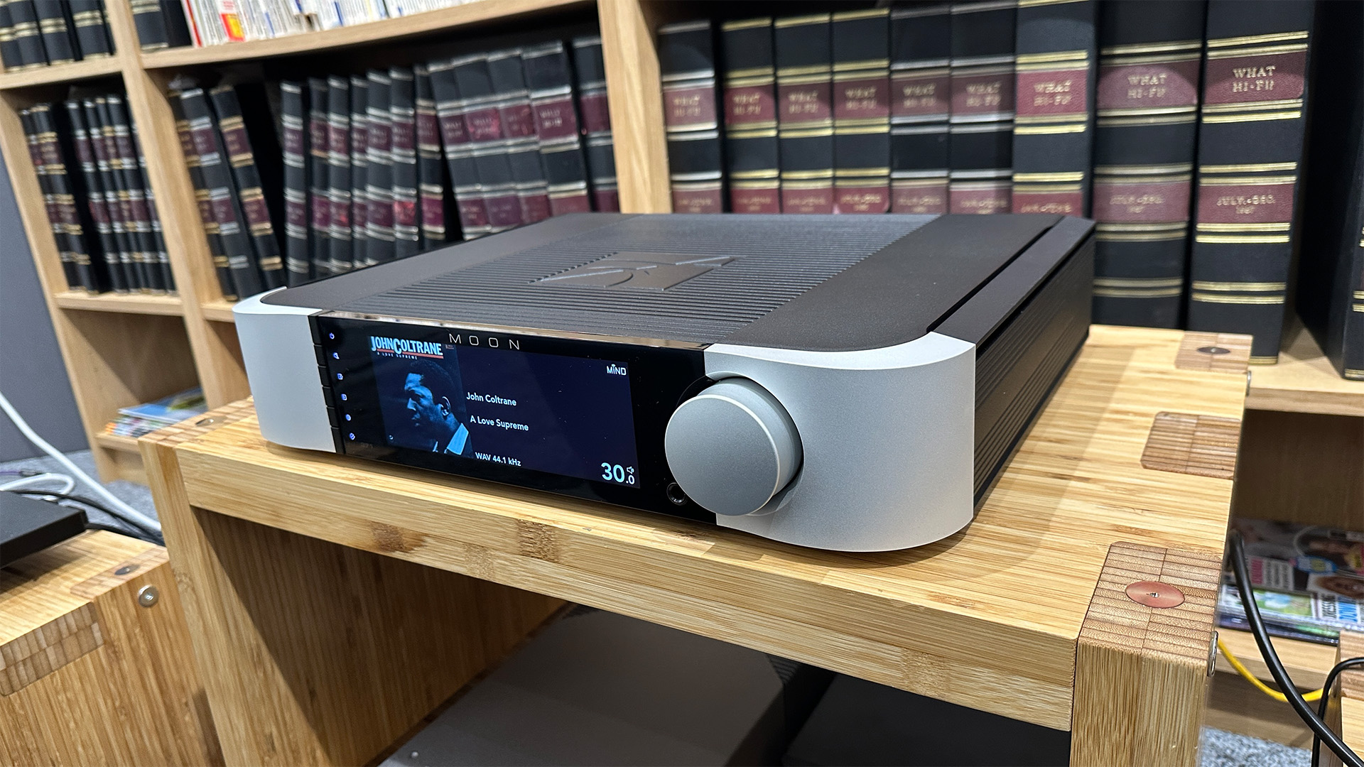 Moon 371 streaming amplifier on wooden hi-fi rack in front of bookcase, on display is John Coltrane