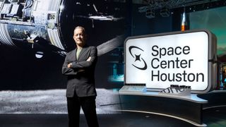 photo of a man wearing a suit standing next to a sign that says "space center houston"