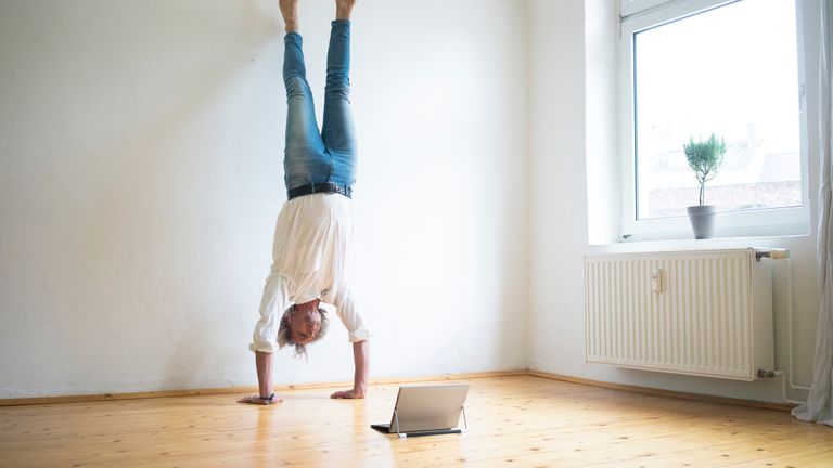 Senior man trying a handstand in front of a laptop