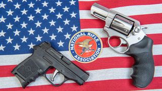 Handguns placed on a US flag beside the logo for the National Rifle Association