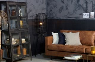 Hurricane Metal Floor Lamp from Cuckooland in a dark, moody living room/man cave with vintage style glass cabinet, brown leather sofa and assorted cushions