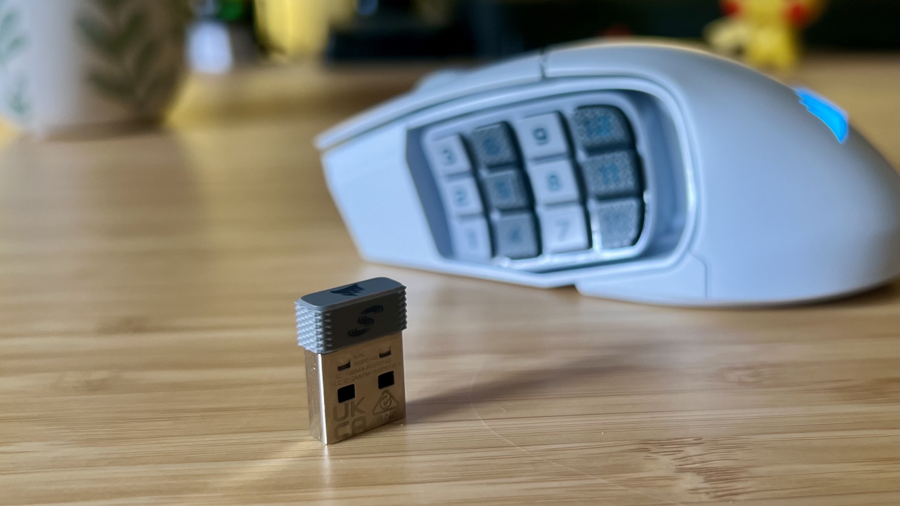 Corsair Slipstream 2.4GHz receiver dongle in front of the Corsair Scimitar Elite Wireless SE gaming mouse on a wooden desk