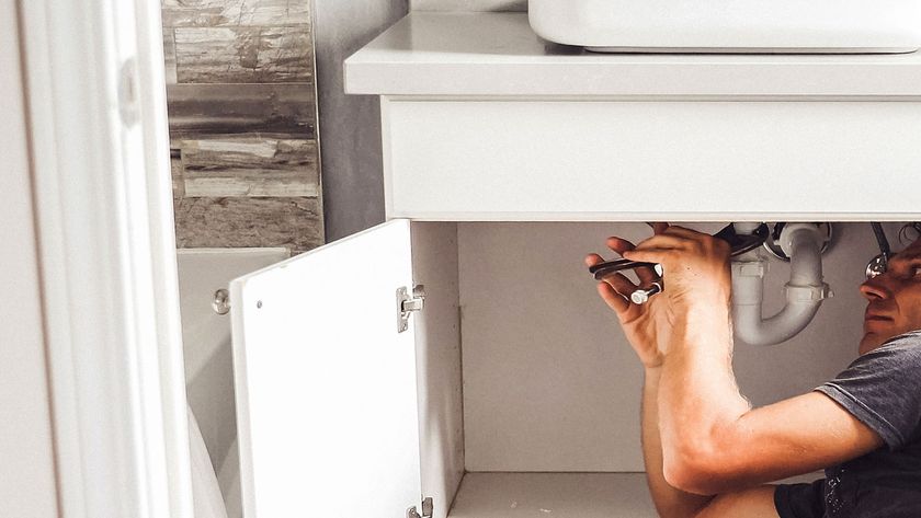 Man under white bathroom sink and cabinet adjusting pipework