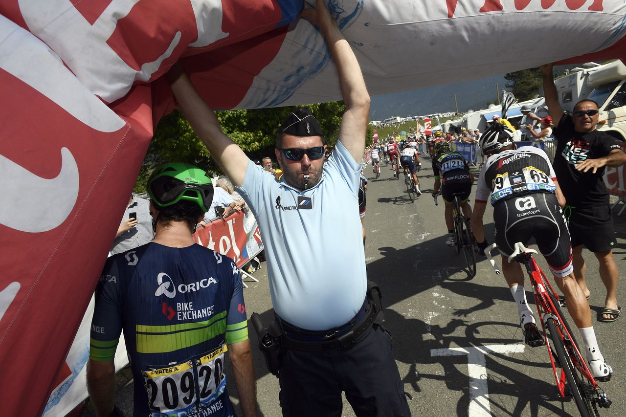 A gendarme helps riders go past the deflated 1km to go banner
