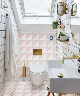 Compact loft style bathroom with floor to ceiling pink and white tiles, brass fittings, and skylight